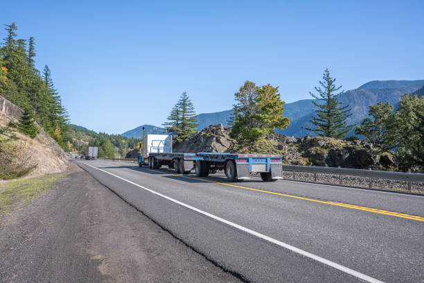 istock Big rig blue classic semi truck transporting two empty flat bed semi trailers going to warehouse for load running on the road along the Columbia Gorge area 1184281438
