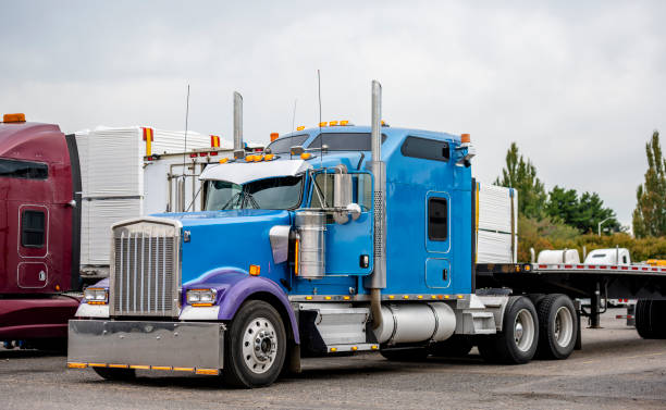 istock Classic big rig blue semi truck with long sleeping compartment and flat bed semi trailer standing on warehouse parking lot 1184283002