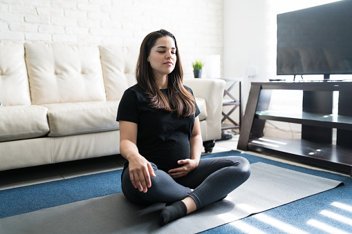 Pretty pregnant woman practicing yoga on exercise mat against sofa at home