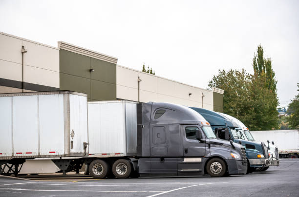 istock Big rig semi trucks with semi trailers standing in the warehouse dock loading cargo for next delivery 1184284761