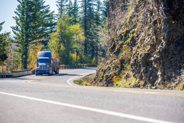 istock Blue big rig semi truck transporting cargo in covered bulk semi trailer turning around the cliff on the winding road with autumn trees 1184284848