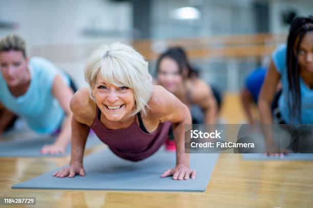 Mujer Senior En Clase Fitness En Una Foto De Stock De Plank Pose Smiling Foto de stock y más banco de imágenes de Ejercicio físico
