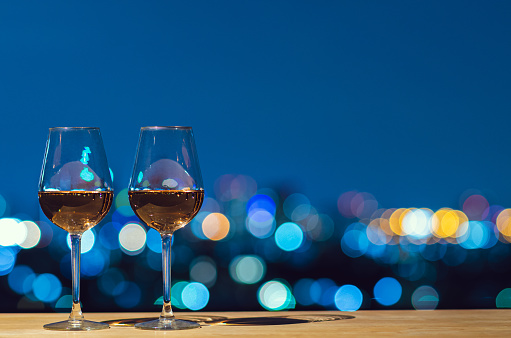 Two glasses of Rose wine with city colorful bokeh light from rooftop building.