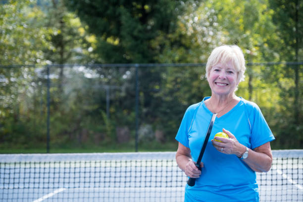 Portrait of an active senior woman An active senior woman enjoys playing pickleball at a public court. She is enjoying her retirement years. Active senior woman outdoors tennis senior adult adult mature adult stock pictures, royalty-free photos & images