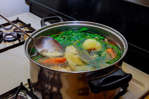 Homemade preparing chicken soup with vegetables in metal pan broth with herbs