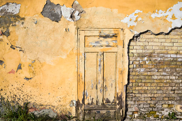 the old brick wall of the house from which part of the plaster has fallen off and destroyed, close-up of an old building during the period of its destruction, closed yellow wooden door