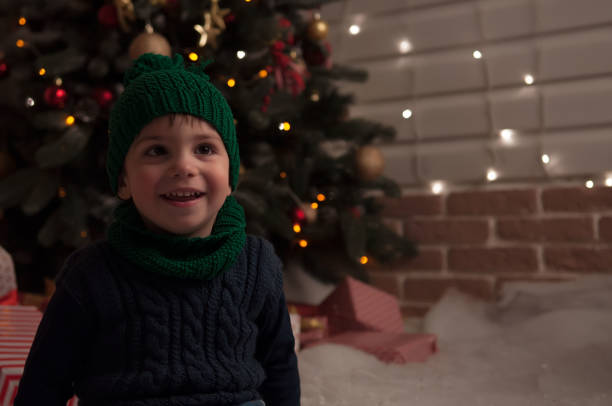 Smiling boy sitting under the Christmas tree with lights.