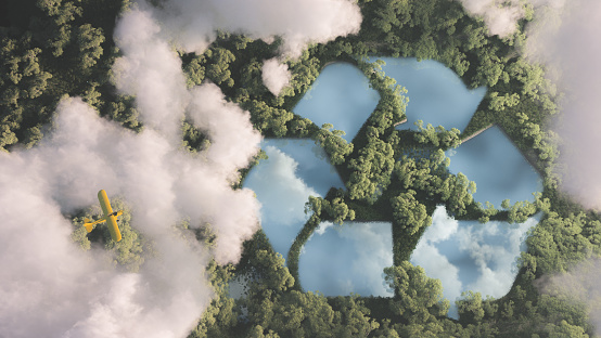 istock Concepto de gestión de residuos ecológico. Señal de reciclaje en forma de lago en medio de la densa vegetación de la selva amazónica vista desde lo alto de las nubes con un pequeño avión amarillo. Renderizado 3d. 1184328778