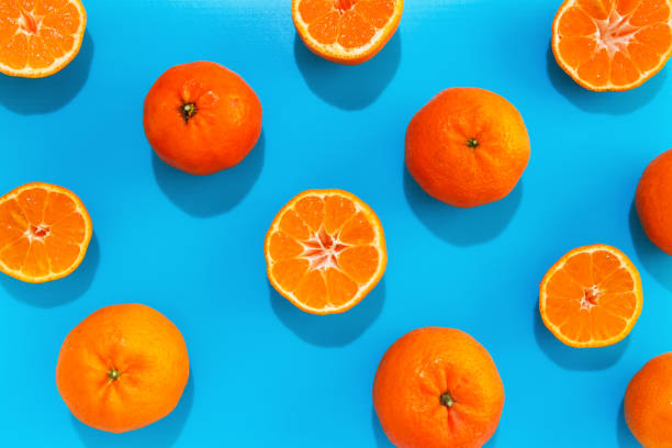 istock Mandarin whole and halves in lines with hard shadows on blue background, flat lay image. 1184328851