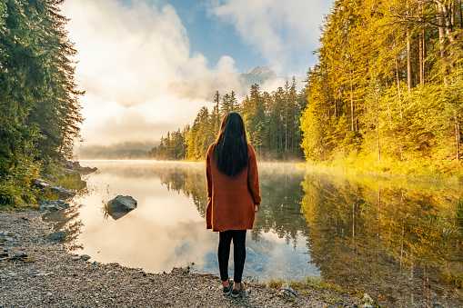 Rear view of a young woman standing by the lake. Scenic surroundings near famous lake Eibsee. Wonderful day gorgeous scene. Location resort Garmisch-Partenkirchen, Bavarian alp, sightseeing Europe. Outdoor activity. Explore the world's beauty.