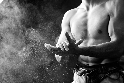 Midsection portrait of muscular man coating his hands in powder chalk magnesium preparing to climb, motion shot with