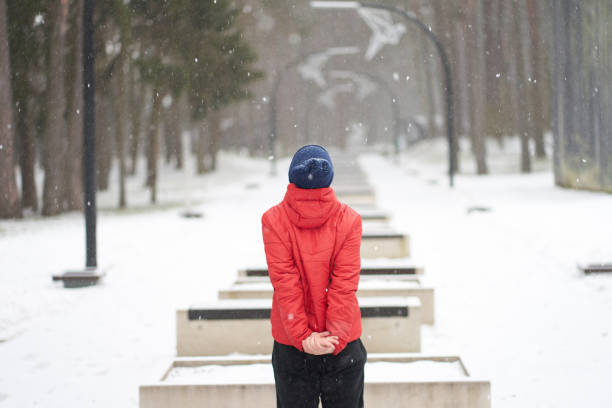 istock Caucasian man dressed in red jacket enjoying snowfall in park, standing backfront 1184342247