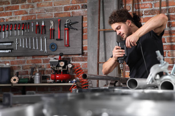 istock man in home workshop garage work drilling metal with drill, repair iron pipe on the workbench full of wrenches, diy and craft concept 1184347971