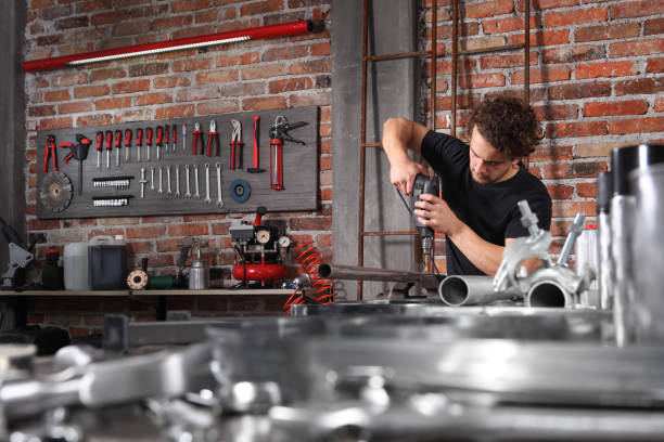 man in home workshop garage work drilling metal with drill, repair iron pipe on the workbench full of wrenches, diy and craft concept - drill red work tool power imagens e fotografias de stock