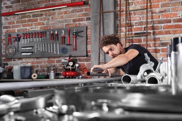 man work in home workshop garage with sandpaper sanding surface of metal pipe on the workbench full of wrenches, diy and craft concept