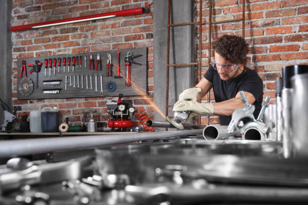 o trabalho do homem na garagem home da oficina com moedor do ângulo, óculos de proteção e luvas da construção, o metal do moedor faz faíscas, diy e conceito do ofício - grinding steel sparks cutting - fotografias e filmes do acervo