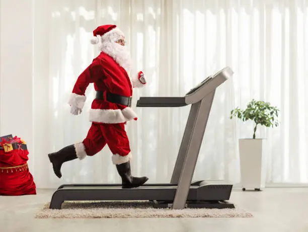 Full length profile shot of Santa Claus running on a treadmill at home
