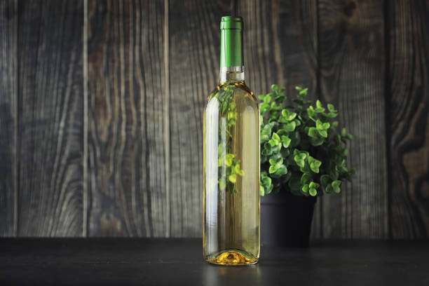 Transparent bottle of white dry wine on the table. White wine glass on a wooden background.