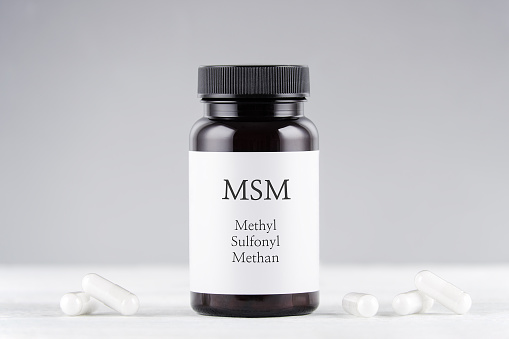 nutritional supplement msm, sulfur, methyl sulfonyl methan bottle and capsules on gray background