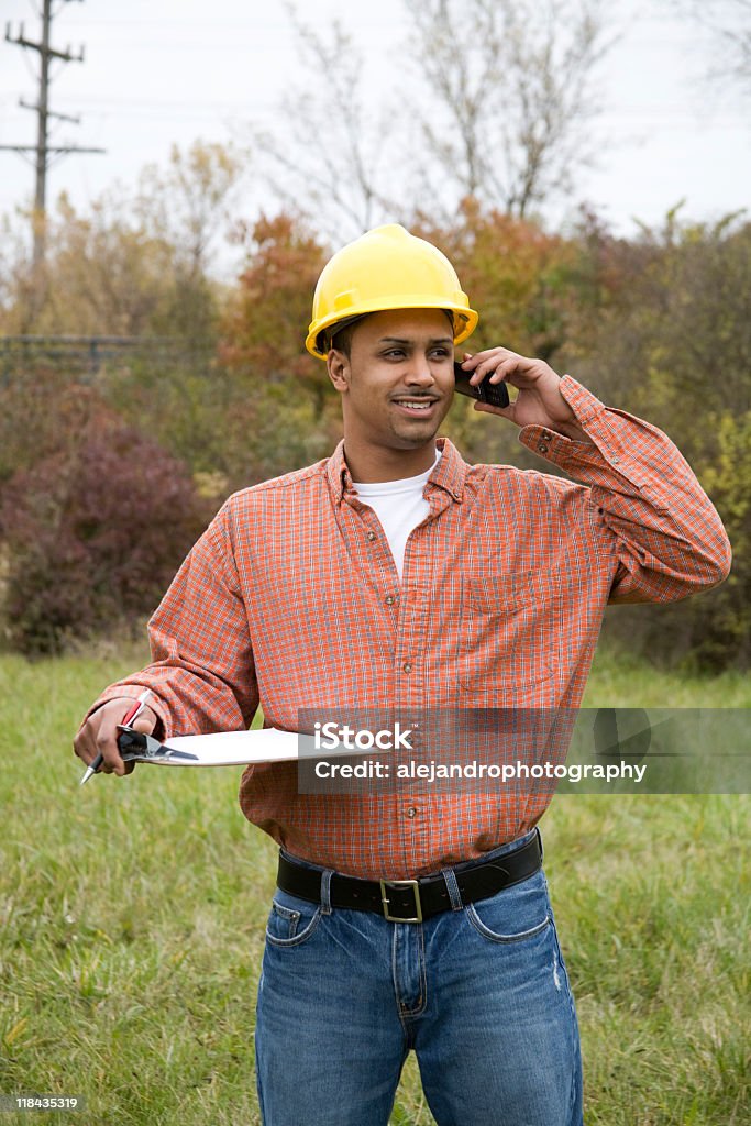 latino costruzione Operaio sorridente sul telefono cellulare - Foto stock royalty-free di Abbigliamento