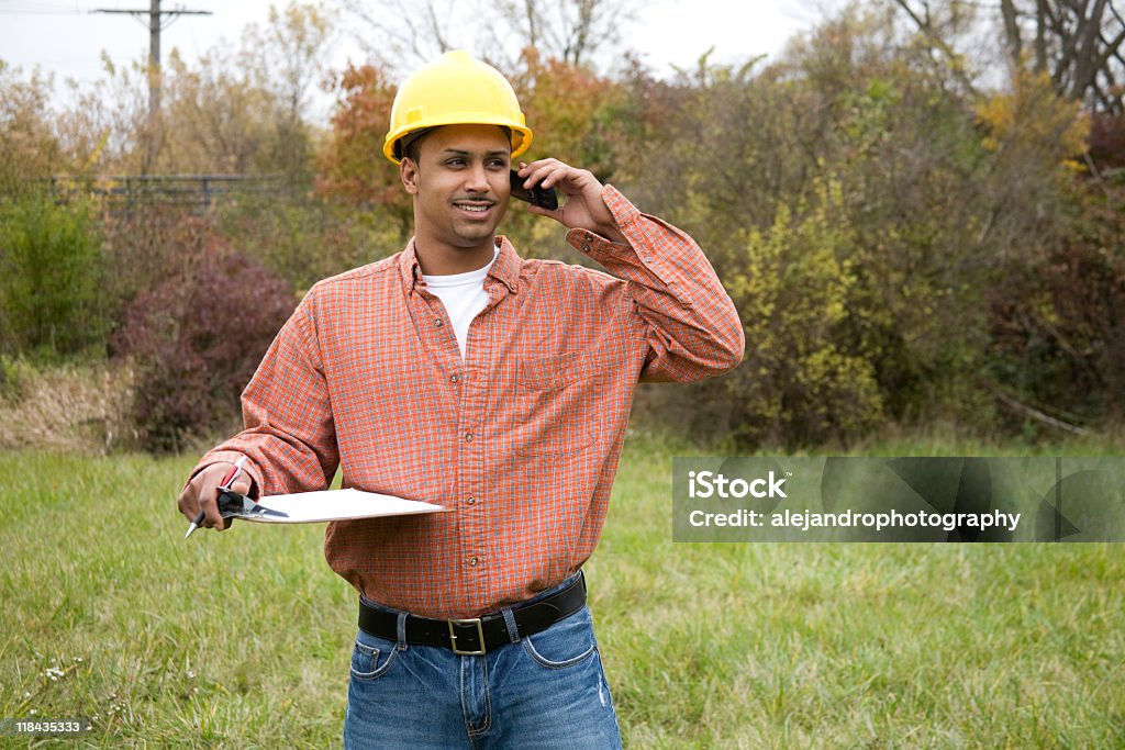 latino construcción trabajador sonriente por teléfono celular - Foto de stock de 20 a 29 años libre de derechos