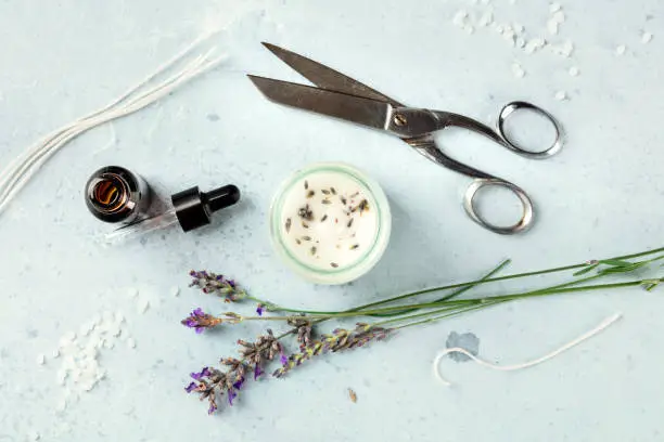 Handmade lavender scented candle with essential oil, flowers, wax, wicks, and scissors, flat lay, overhead shot. An artisanal Christmas gift
