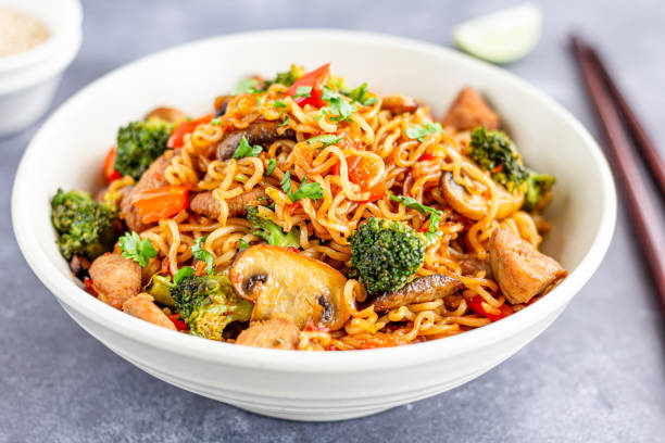 Stir-Fried Noodles Close-Up Ramen Noodles with Broccoli, Bell Pepper, Mushroom, and Chicken in a Bowl with Chopsticks Close Up Photo. stir fried stock pictures, royalty-free photos & images