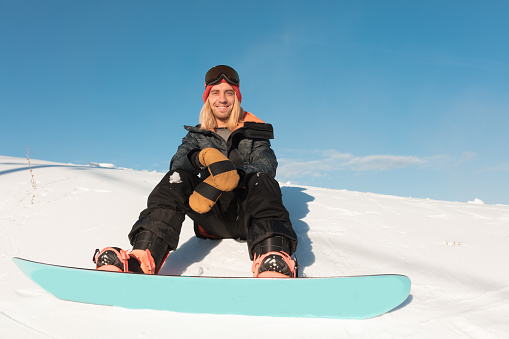 smiling positive sportsman looking at the camera. good day for snowboarding.man rejoicing at useful unforgettable weekends.low view photo