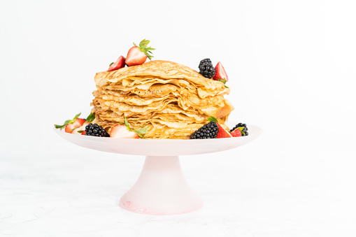Stack of freshly baked crepes with berries on a cake stand.