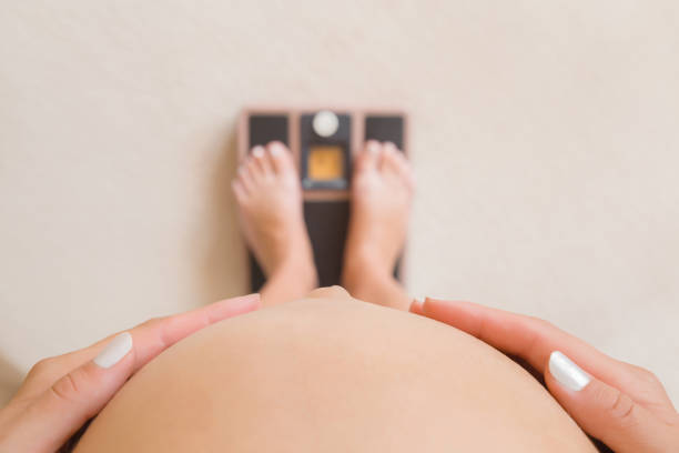 femme enceinte restant sur des balances de poids. occupe-toi du corps. mains touchant le grand ventre nu. fermez-vous vers le haut. point de vue tiré. vue du haut. - grand view point photos et images de collection