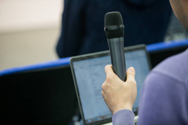 istock The main speaker is holding the black wireless microphone by the left hand and perform lecture in the class with blurred background, speaking, learning, teaching, academic, study concept. 1184370834