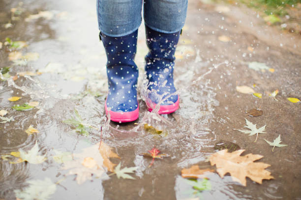 istock Woman in blue rubber boots jumping in puddle 1184371552