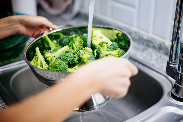 istock Woman washing broccoli in the kitchen sink 1184372746