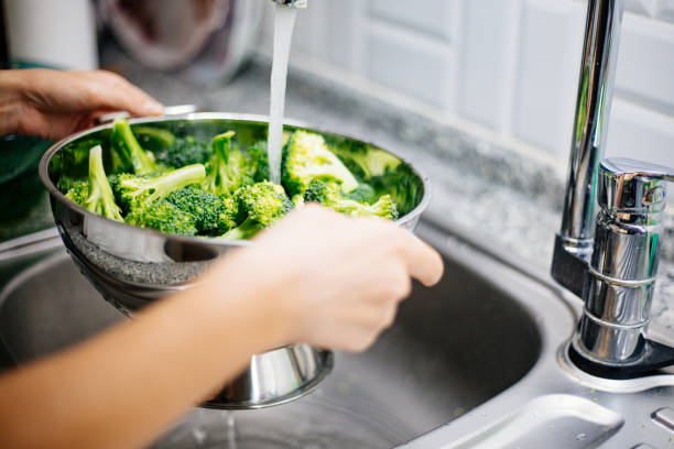 donna lava broccoli nel lavandino della cucina - mature adult immagine foto e immagini stock