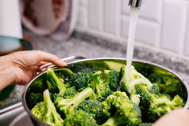 istock Woman washing broccoli in the kitchen sink 1184373043