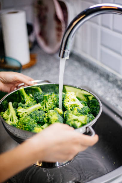 istock Woman washing broccoli in the kitchen sink 1184373129