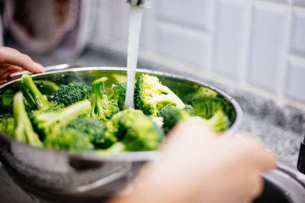 istock Woman washing broccoli in the kitchen sink 1184373253