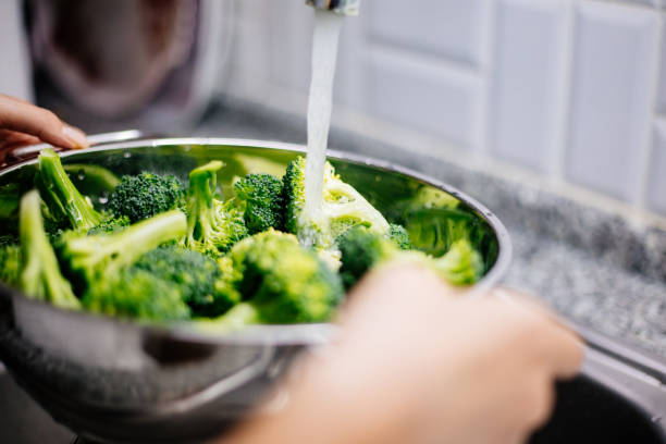 istock Woman washing broccoli in the kitchen sink 1184373273