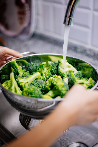 istock Woman washing broccoli in the kitchen sink 1184373346