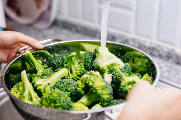 istock Woman washing broccoli in the kitchen sink 1184373350