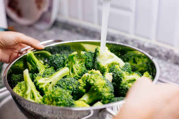 istock Woman washing broccoli in the kitchen sink 1184373375