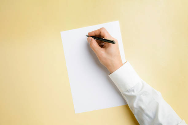 istock Male hand holding pen and writing on empty sheet on yellow background for text or design 1184374784