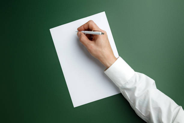 istock Male hand holding pen and writing on empty sheet on green background for text or design 1184374788