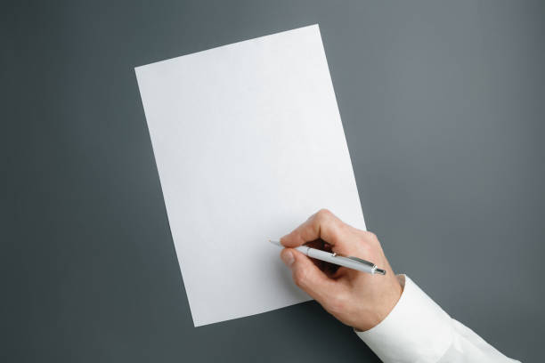 istock Male hand holding pen and writing on empty sheet on grey background for text or design 1184374847