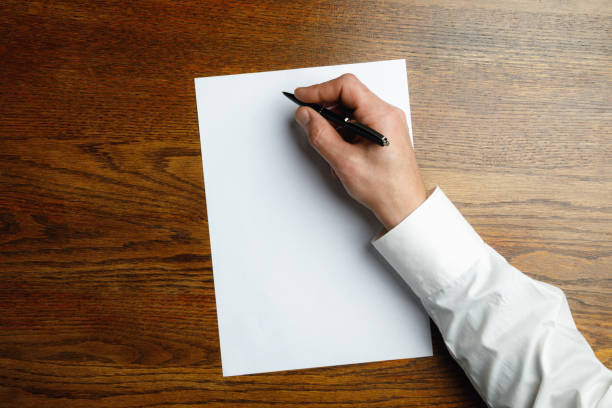 istock Male hand holding pen and writing on empty sheet on wooden background for text or design 1184374867