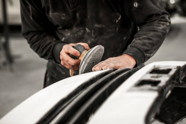 Body repair technician removing excess filling from an accident-damaged car bumper using a pneumatic sander Car repair technician using a pneumatic sanding tool to remove excess filling form a car number that got damaged in accident. door panel stock pictures, royalty-free photos & images