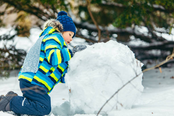 istock little cute boy making snowman. rolling big snowball. winter leisure 1184375347