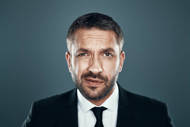istock Charming young man in full suit looking at camera while standing against grey background 1184375442