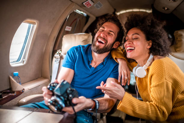 famosa joven riendo y señalando a su pareja en una cámara dslr mientras se sienta juntos a bordo de un avión privado - status symbol audio fotografías e imágenes de stock