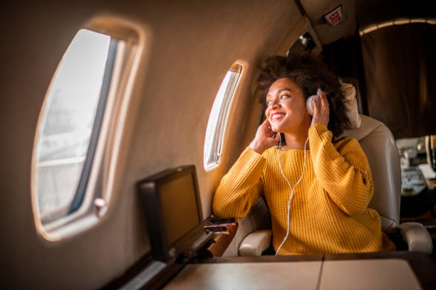 istock Young chic woman sitting on a private airplane and looking through window while listening to music through headphones 1184376411